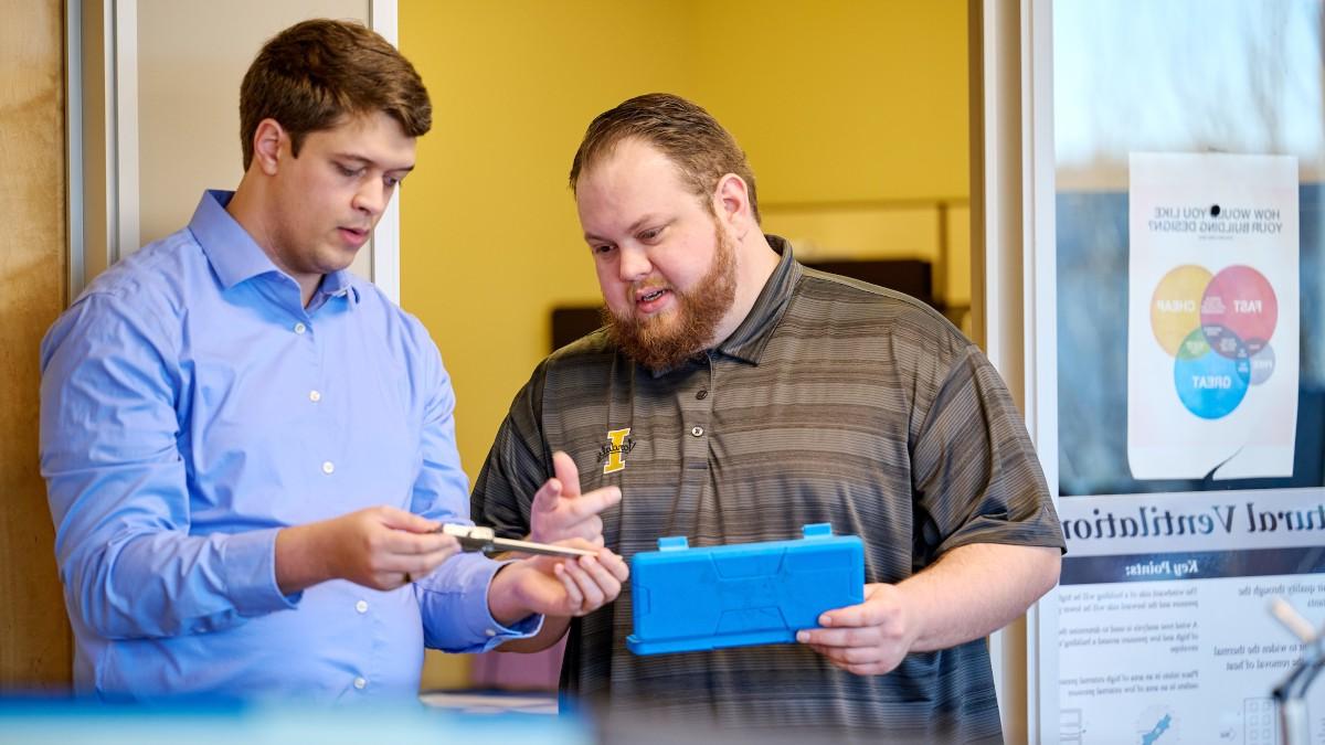 Two staff members discuss a tool in the integrated design lab. 