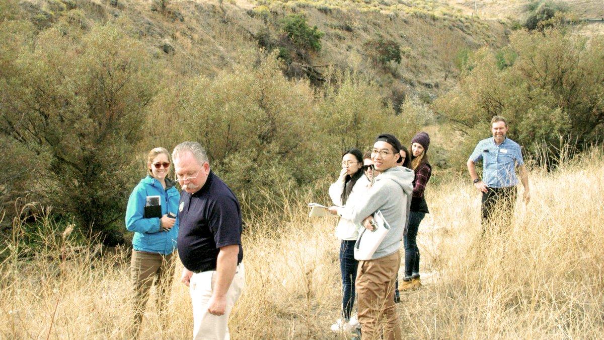 Students and faculty stand in a group in an area of wild grass with hills rising behind them.