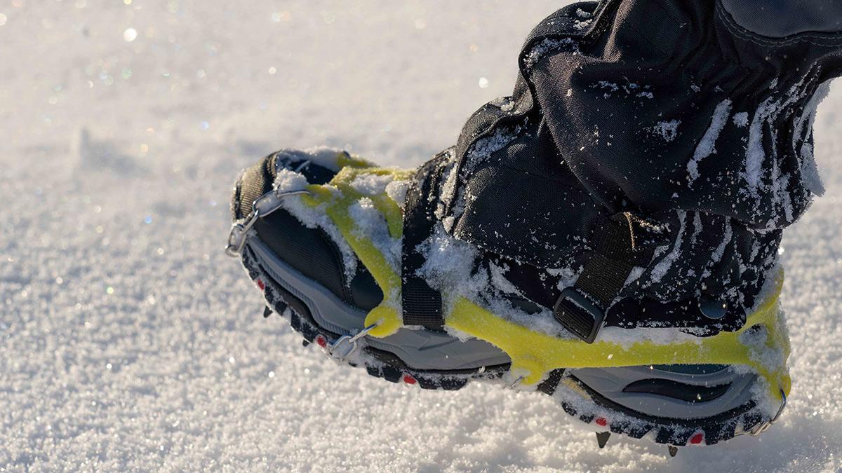 A shoe with traction device affixed, poised to step into snow.