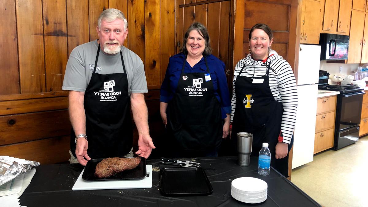 Three people stand in front of table with roast.